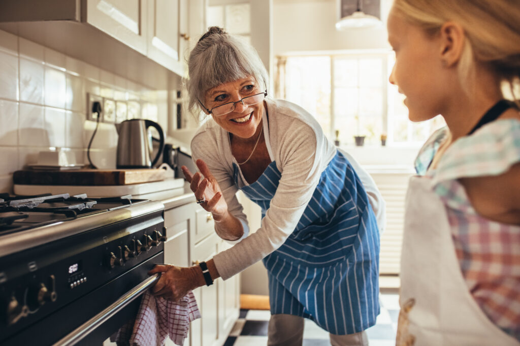Oma kijkt naar haar kleindochter in de keuken en houd met haar hand de ovenhendel vast.