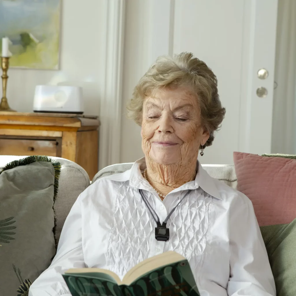 Oudere vrouw met CSI alarmknop om de hals leest op de bank