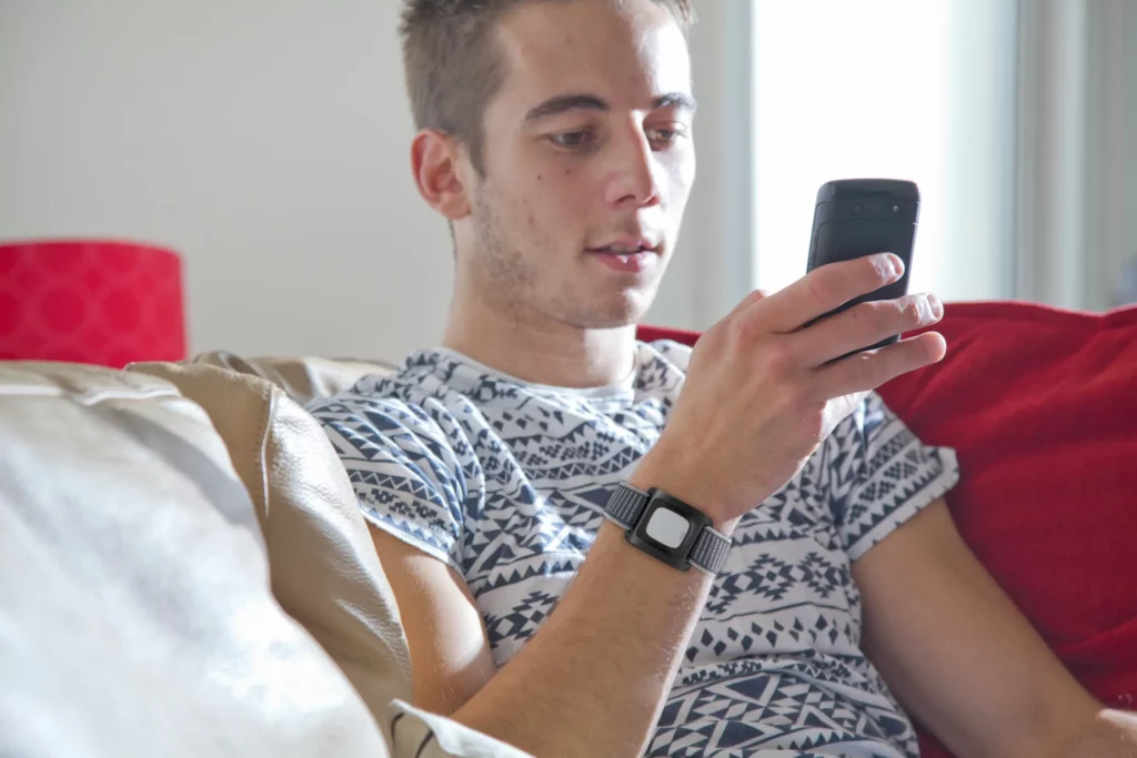 Jonge man zit op de bank met alarm armband van CSI Persoonsalarmering om